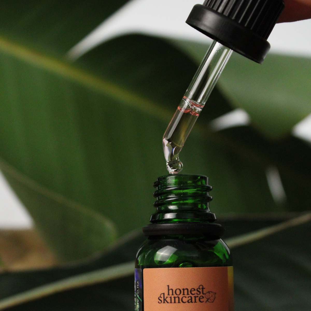 Dropper dispensing rosemary essential oil benefits from a green bottle surrounded by leaves.