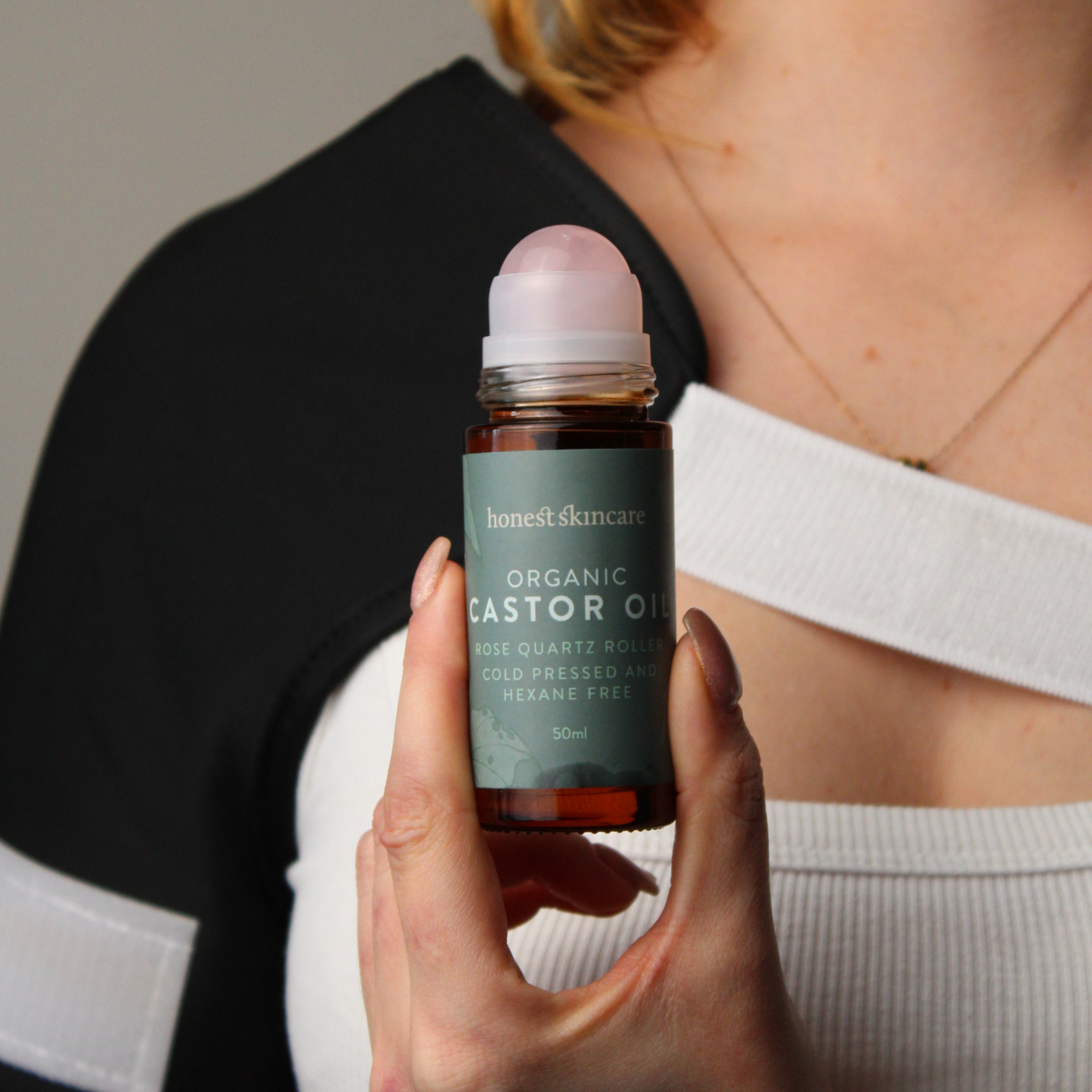 Rose Quartz Roller with Certified Organic Castor Oil held by a person, showcasing skin care benefits and packaging.