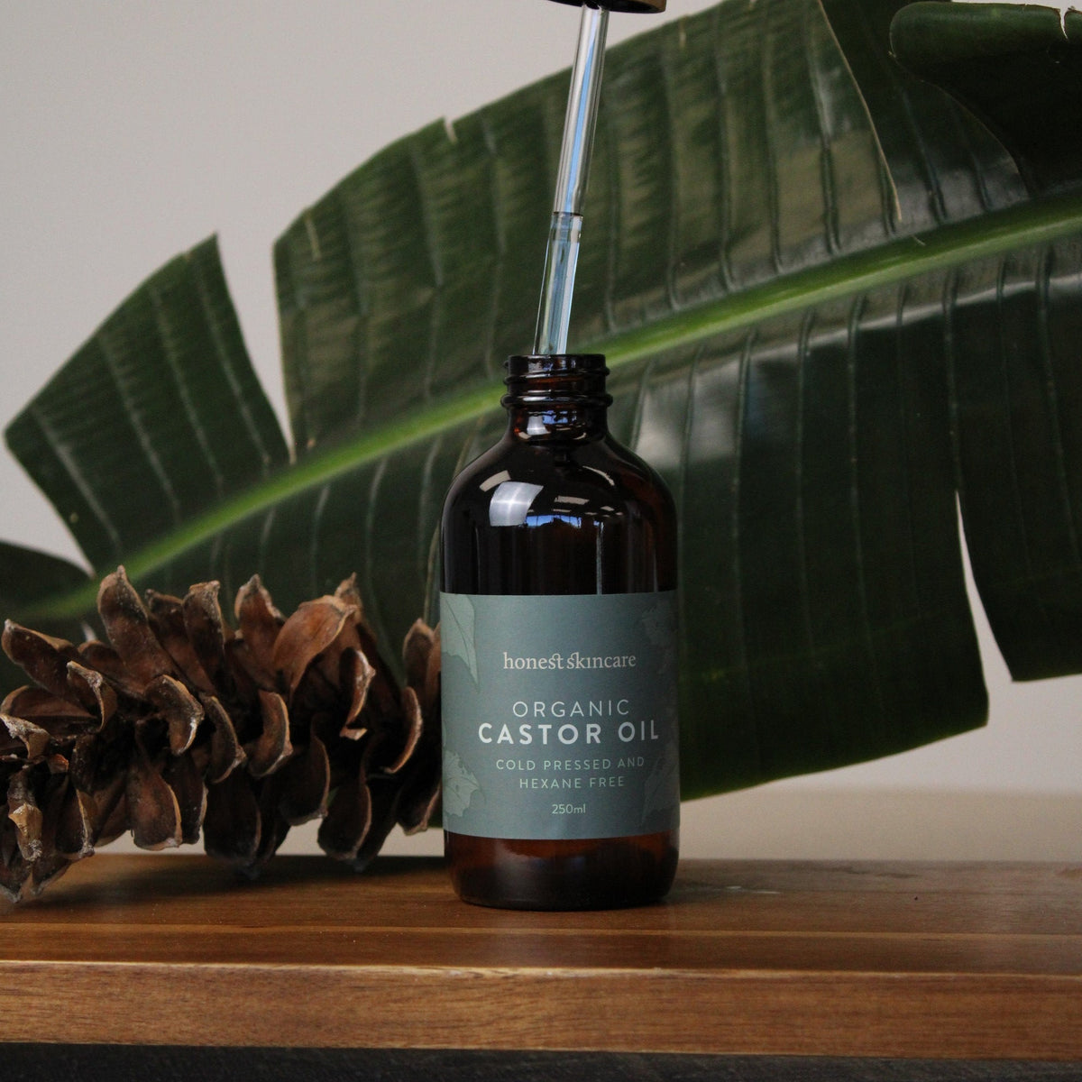 Organic castor oil bottle on a wooden surface with greenery, for inflammation and joint care.