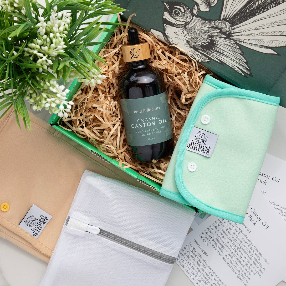 Bottle of organic castor oil with a green label, a small green pouch, and a plant in a decorative box.