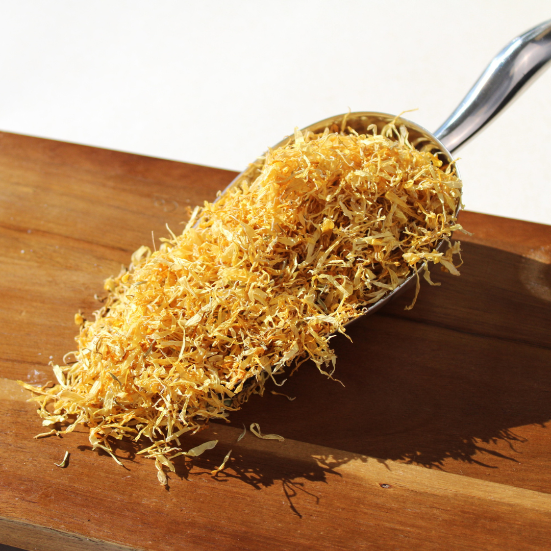 Organic dried calendula petals in a measuring spoon on a wooden surface, highlighting their vibrant yellow color.
