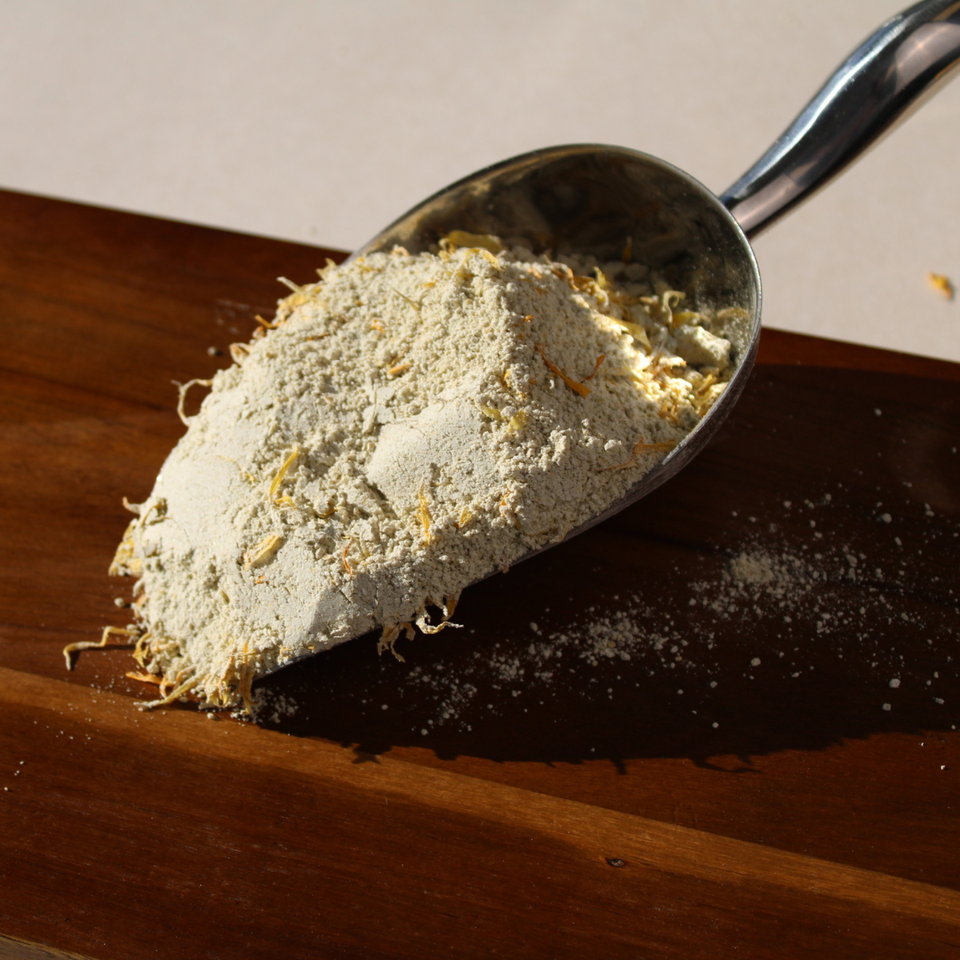 Colloidal oat bath soak with kawakawa, chamomile, and calendula in a metal scoop on a wooden surface.