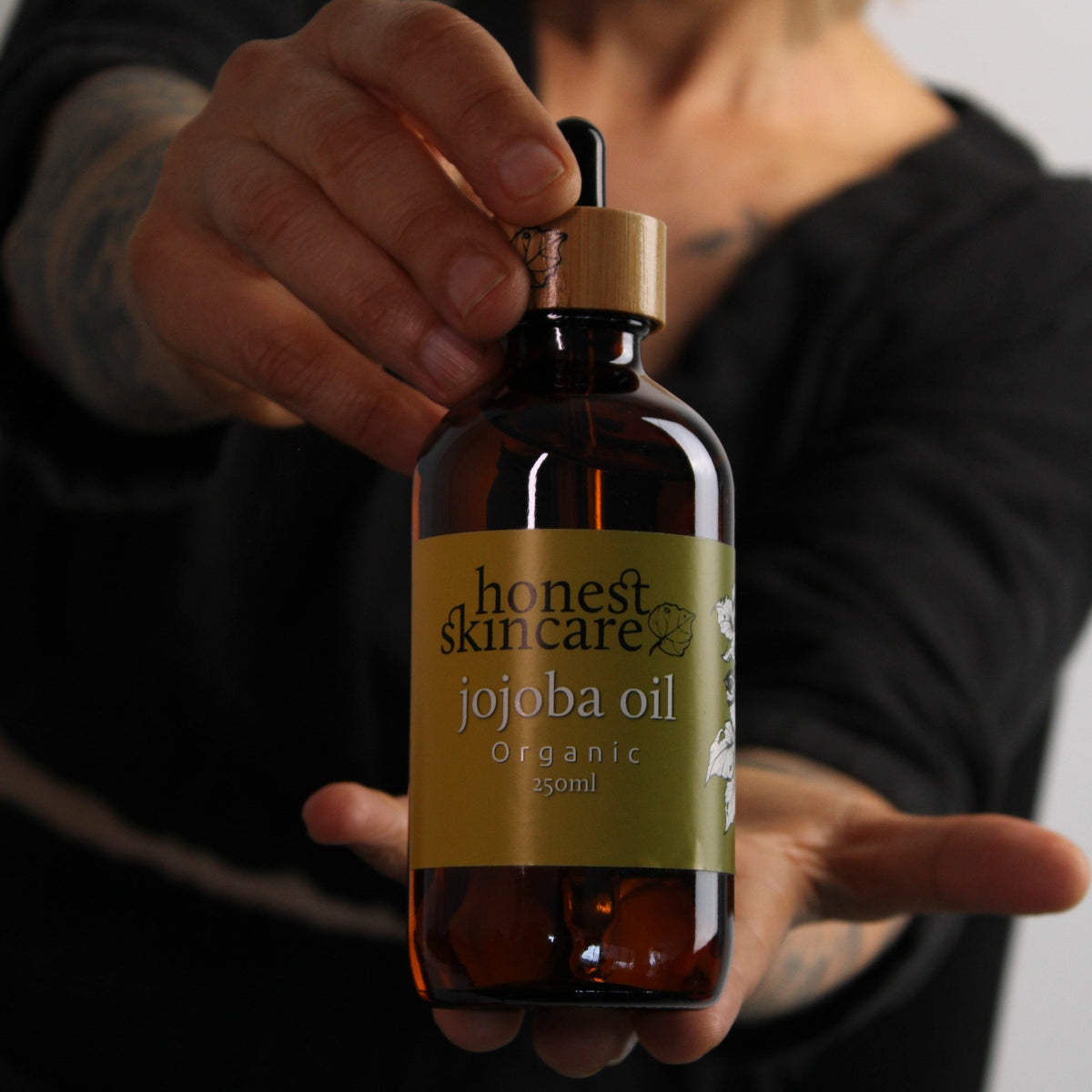 Honest Skincare jojoba oil for skin in amber glass bottle, certified organic 250ml, held by person.