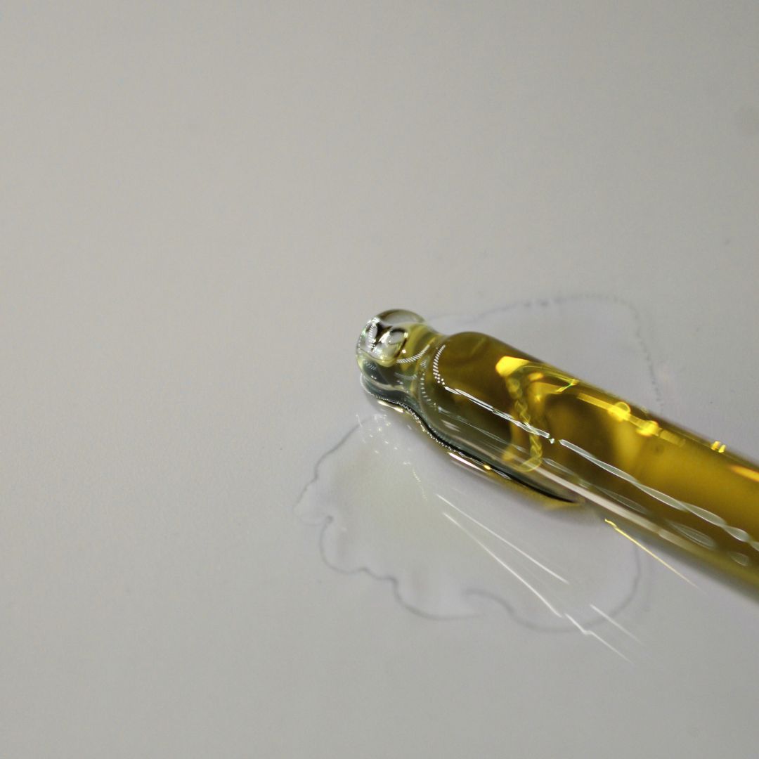Dropper with cold pressed hemp seed oil on a white background, showcasing its rich golden color and lightweight texture.