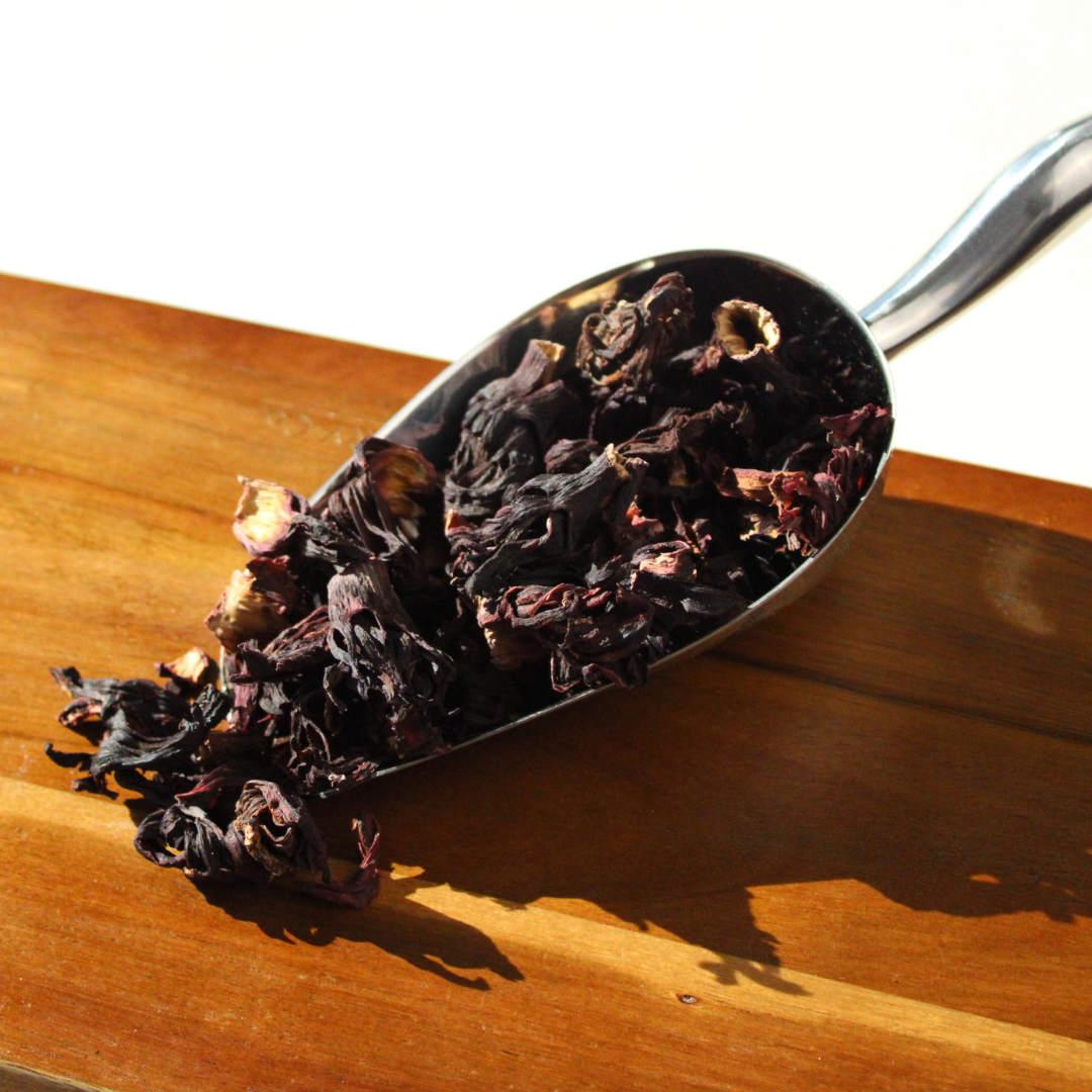 Dried Hibiscus Tea leaves in a metal scoop on a wooden surface