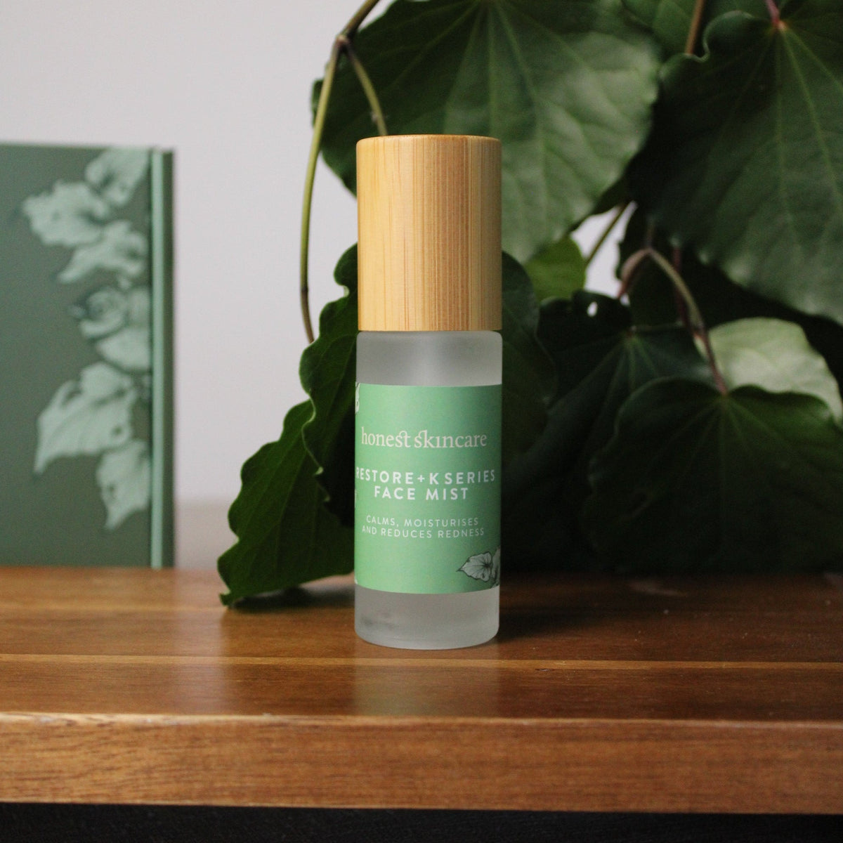 Restore+ K Series Face Mist bottle surrounded by kawakawa leaves on a wooden surface.