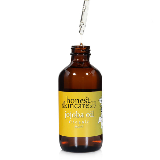 Jojoba Oil for Skin in an amber bottle, dropper releasing organic oil for moisturizing benefits.