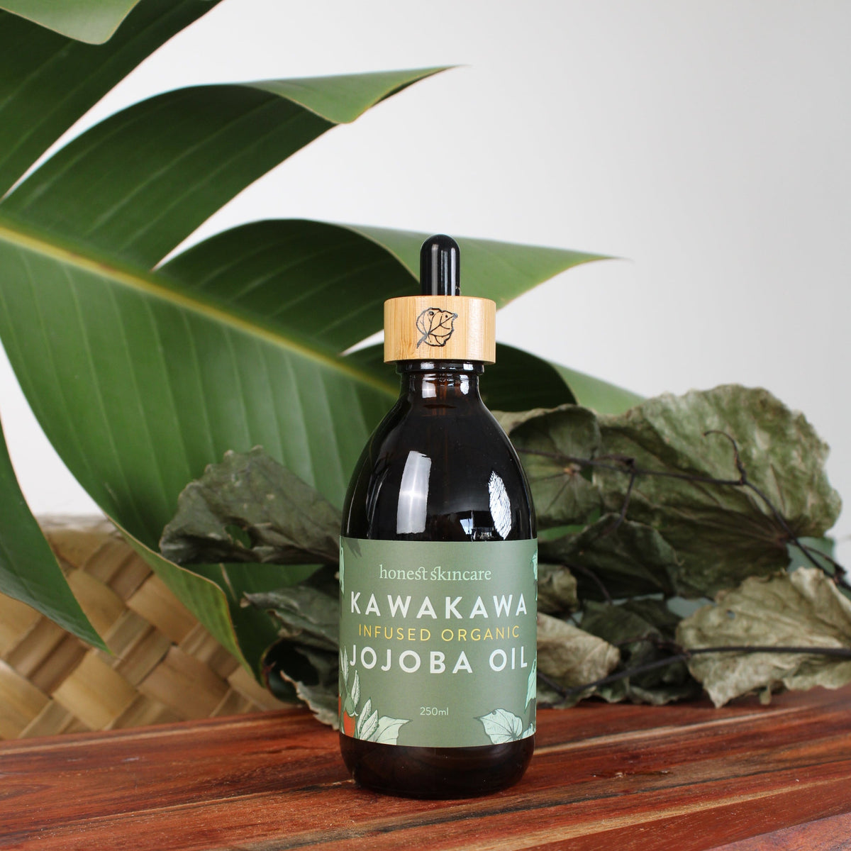 Bottle of Kawakawa Jojoba Oil for Skin - Organic with tropical leaves in the background.