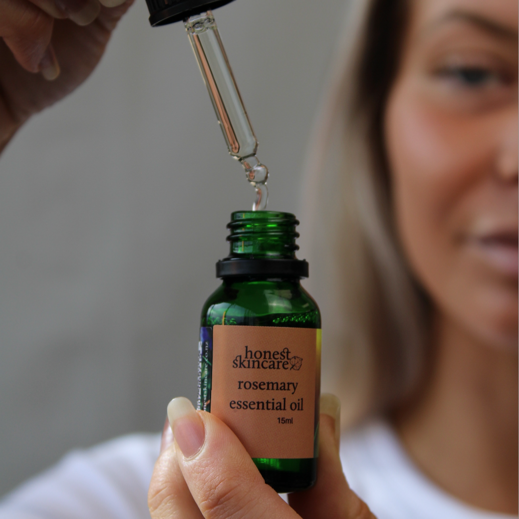 Person holding a dropper above a green bottle of rosemary essential oil benefits.
