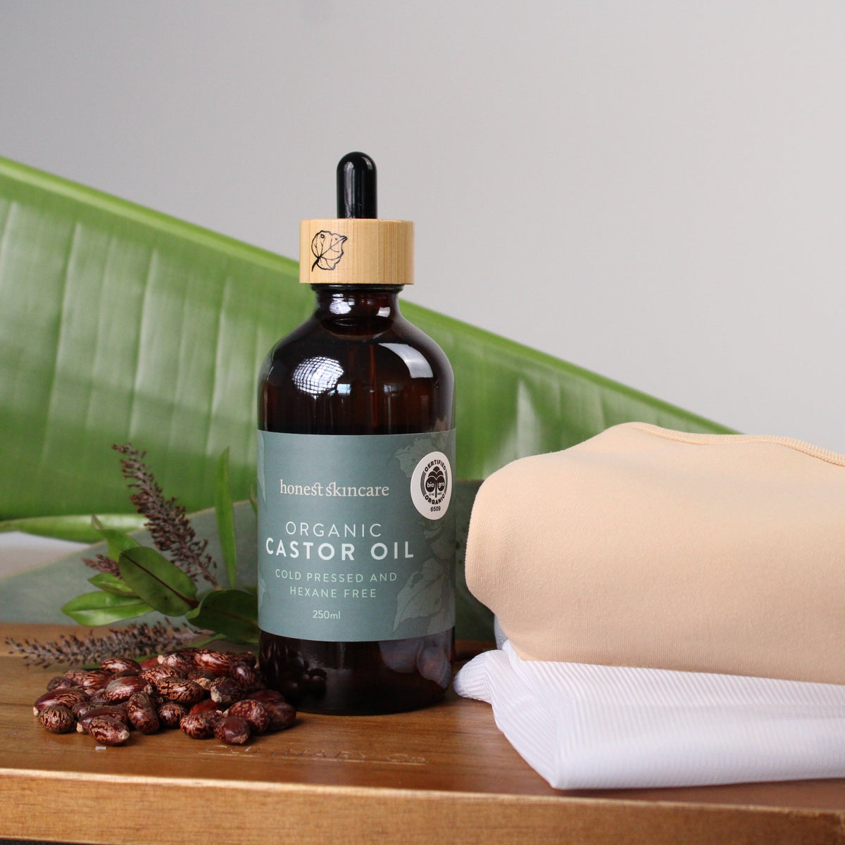 Bottle of organic castor oil with a dropper on a wooden surface with a beige towel and green leaves in the background.