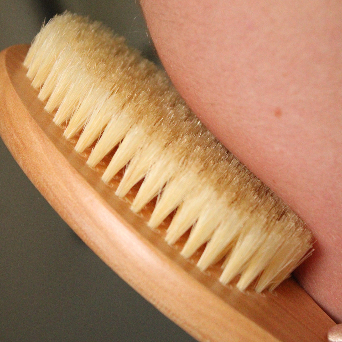 Castor Oil Detox Kit Wooden natural bristle dry brush being used on a person's skin.