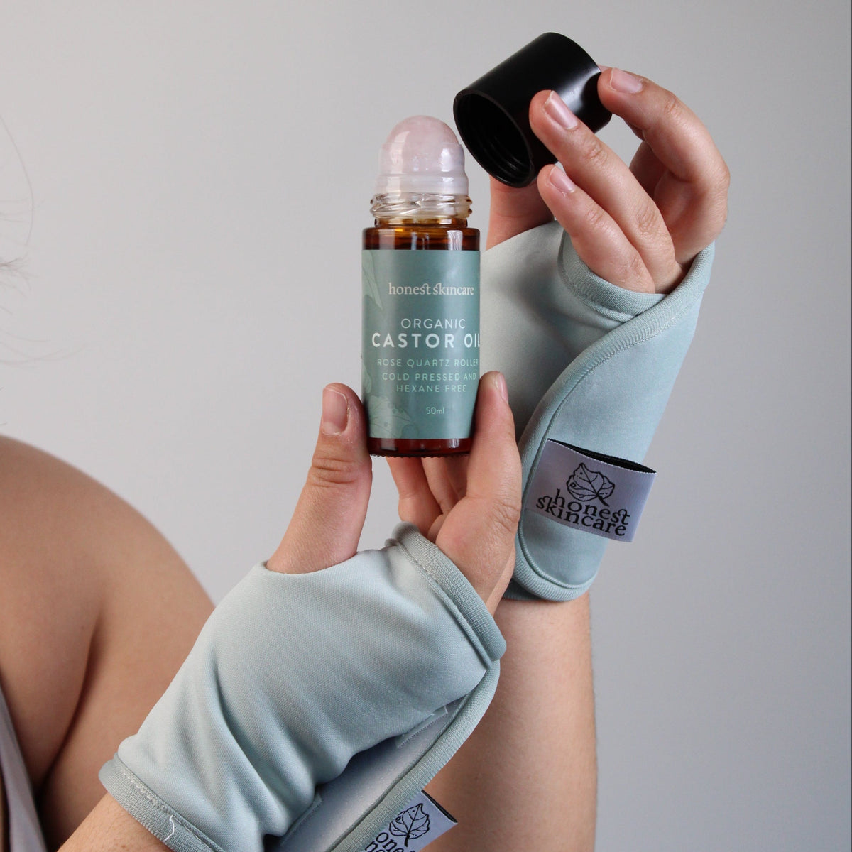 Hand and Wrist Wraps being worn and holds a roll-on bottle of castor oil with its cap off, set against a plain light gray background.