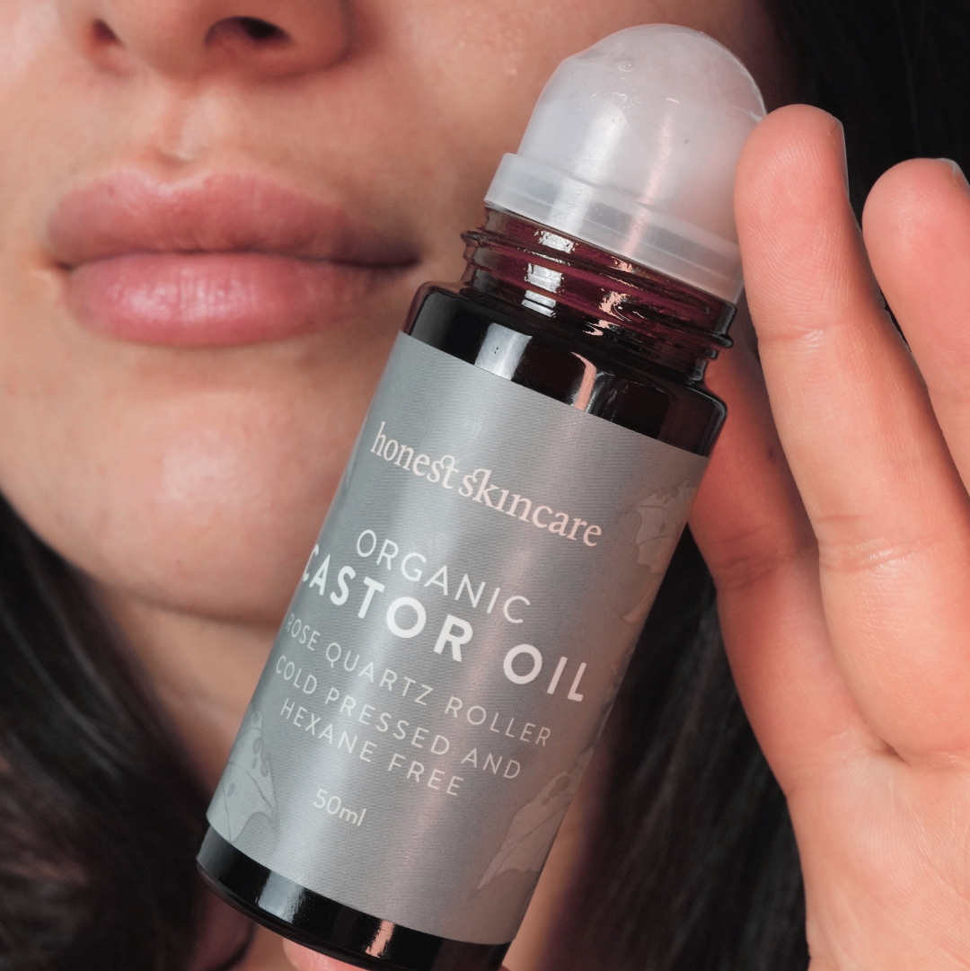 Rose Quartz Roller with Certified Organic Castor Oil being held with a persons face in the background
