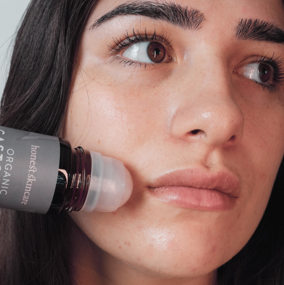 Woman using Rose Quartz Roller with Certified Organic Castor Oil on her face for soothing skincare.