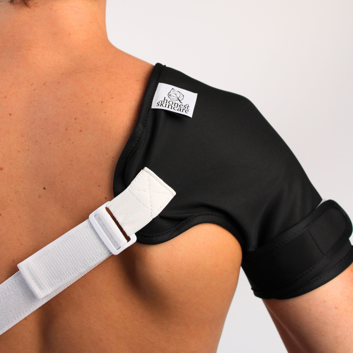 castor oil shoulder pack with a white strap on a person's shoulder, featuring a honest skincare label.