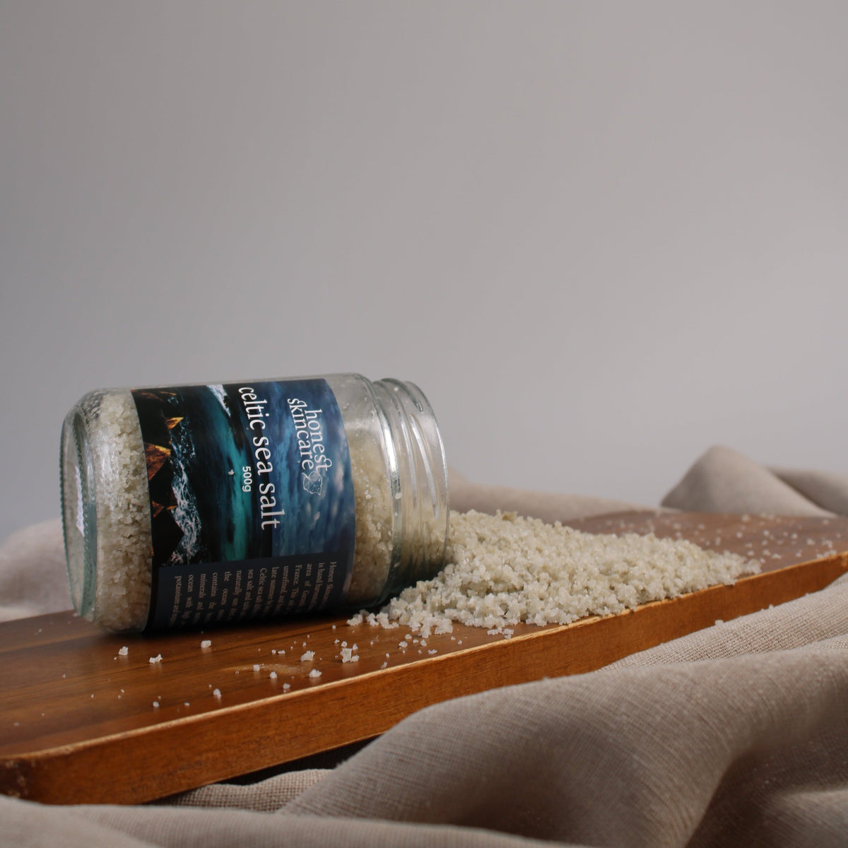 Celtic sea salt in a jar spilling onto a wooden surface, showcasing its natural texture and quality.