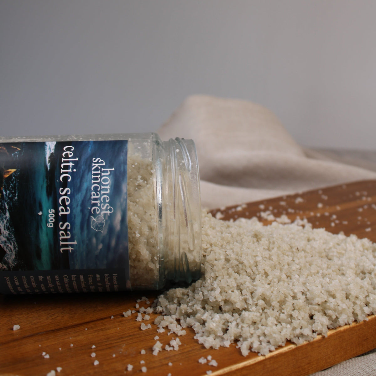 Celtic sea salt in a jar spilled onto a wooden surface, showcasing its coarse, mineral-rich crystals.