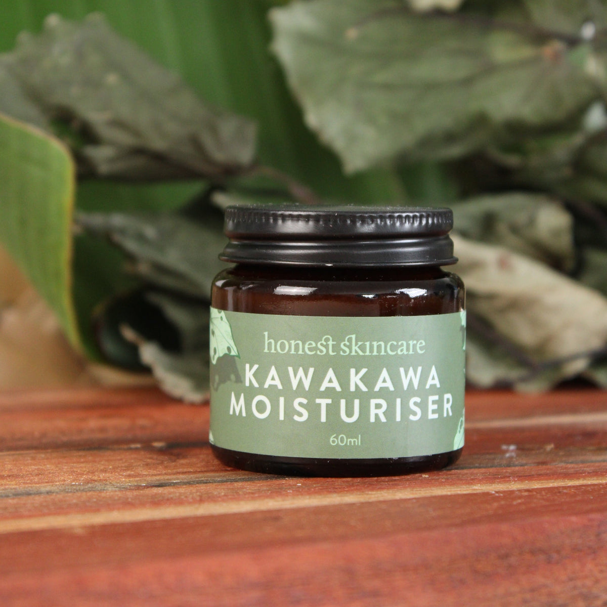 Jar of Kawakawa Moisturiser against a wooden background with green leaves.