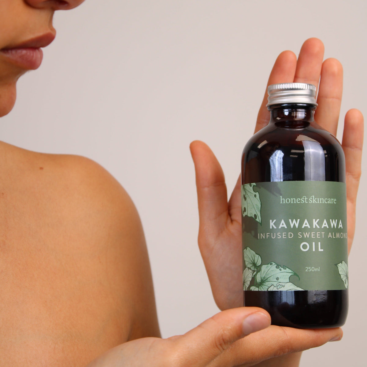 Sweet almond oil for skin in a bottle held by a model, showcasing Kawakawa infusion.