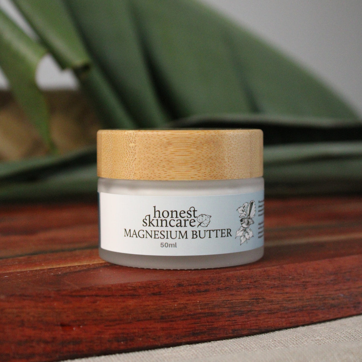 Magnesium butter for sleep in a natural skincare jar on a wooden surface with green leaves in the background.