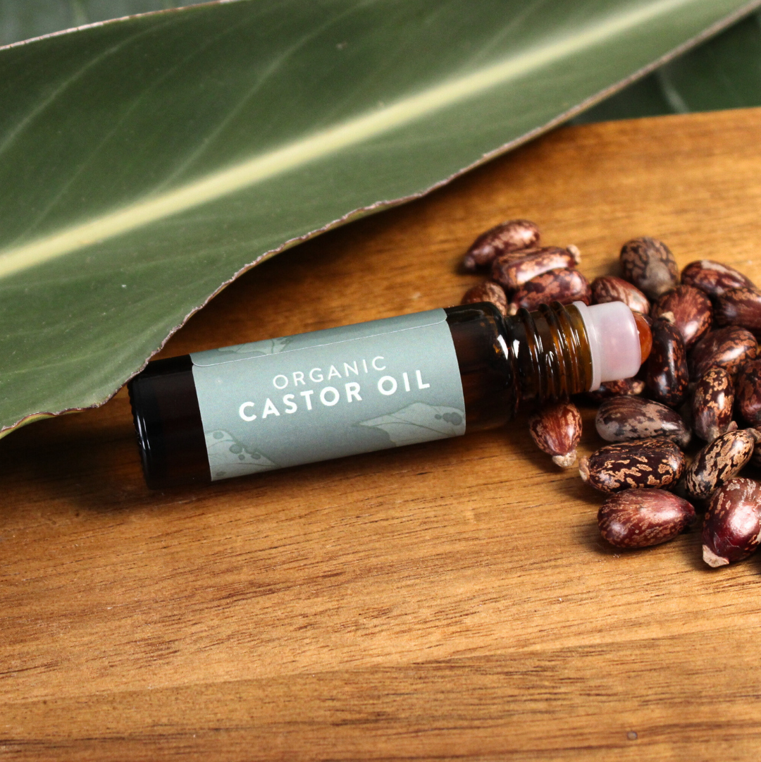Organic Castor Oil Mini Roller bottle on a wooden surface with castor beans and green leaf.