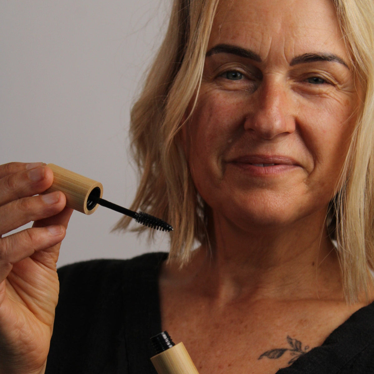 Woman holding a bamboo castor oil applicator, promoting castor oil for eyelashes for fuller and healthier lashes.