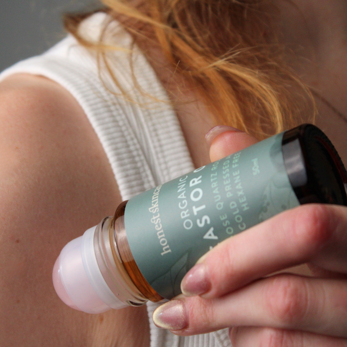 Hand holding a bottle labeled Rose Quartz Roller with Certified Organic Castor Oil with a blurred background