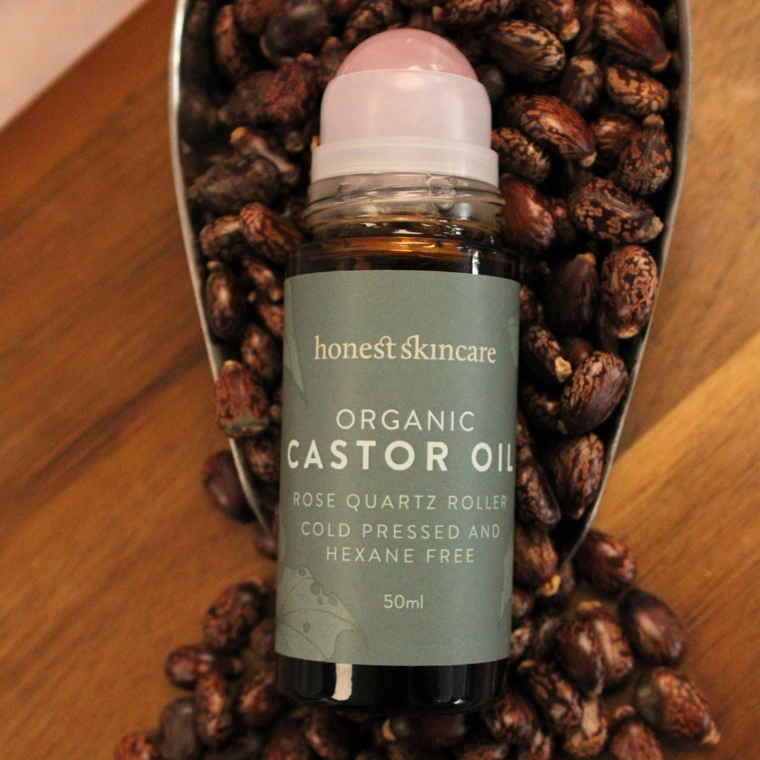 Organic castor oil bottle with rose quartz roller on a wooden surface with seeds.