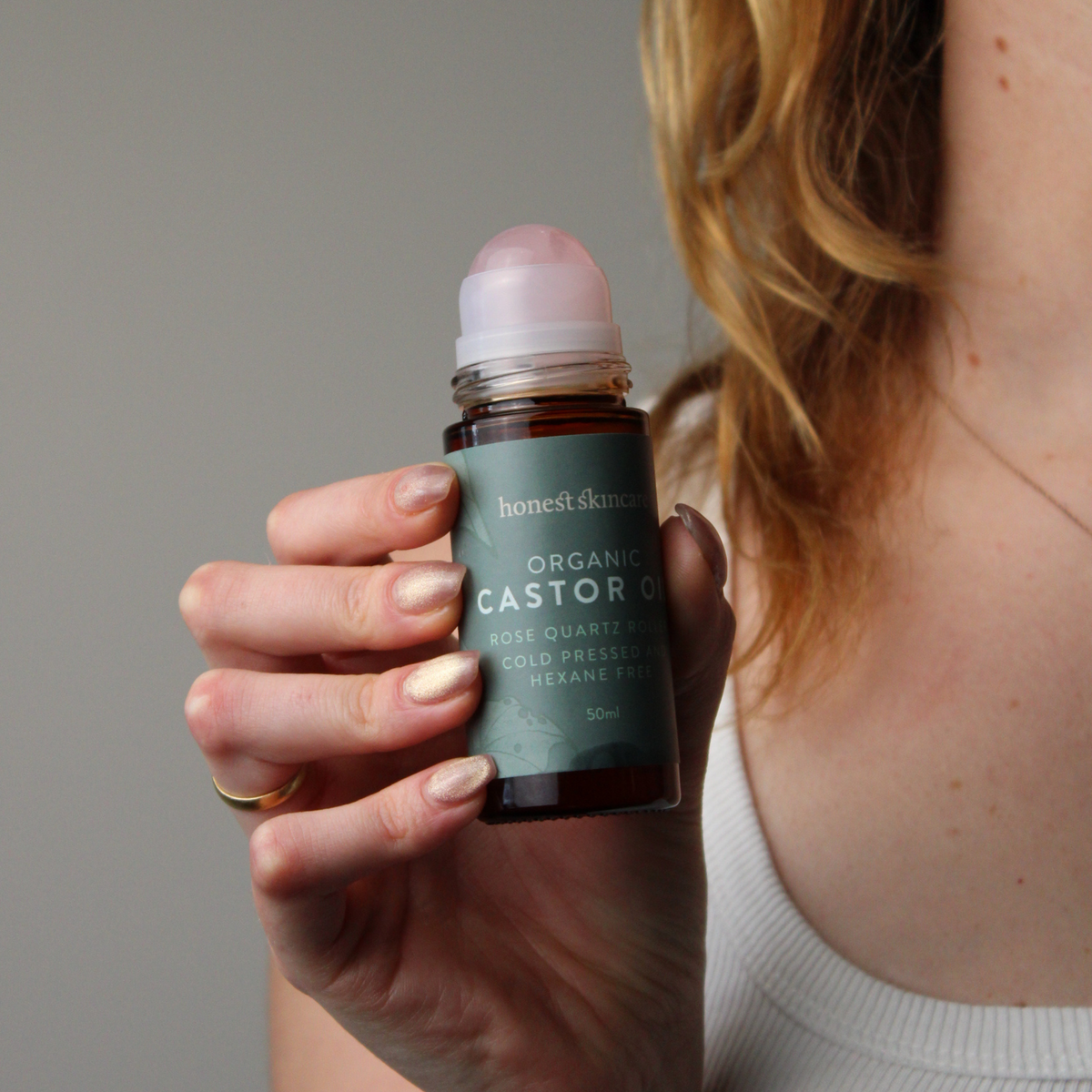Rose Quartz Roller with Certified Organic Castor Oil in a person's hand for skincare routine.