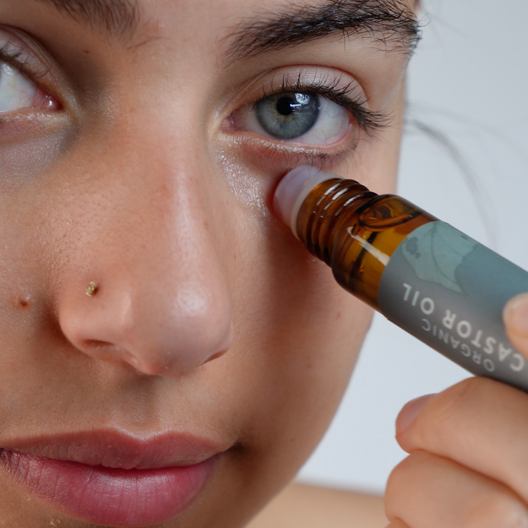A person applying organic castor oil mini roller under their eye for skincare benefits.